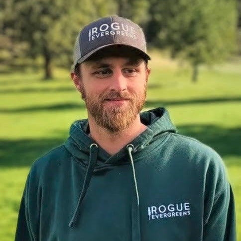 Man wearing a green hoodie and cap with 'Rogue Evergreens' logo in a grassy outdoor setting