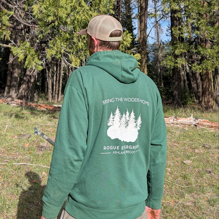 Person wearing a green hoodie with a logo, standing in a forest.