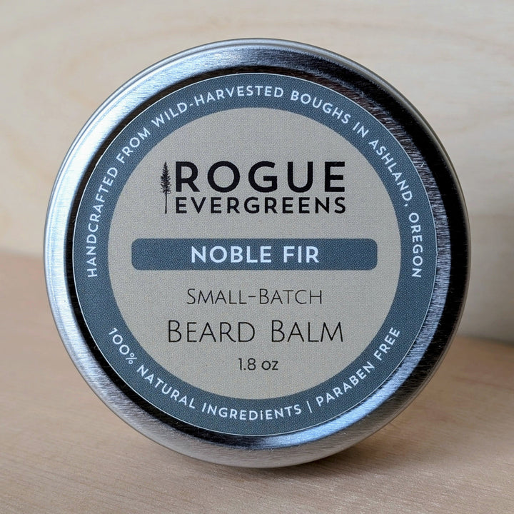 Beard balm container with 'Rogue Evergreens' label on a wooden surface